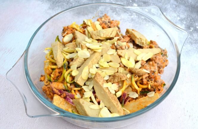 Glass bowl containing vegetarian Quorn sliced roast fillets on top of grains, spiralised courgette in a curried yoghurt sauce