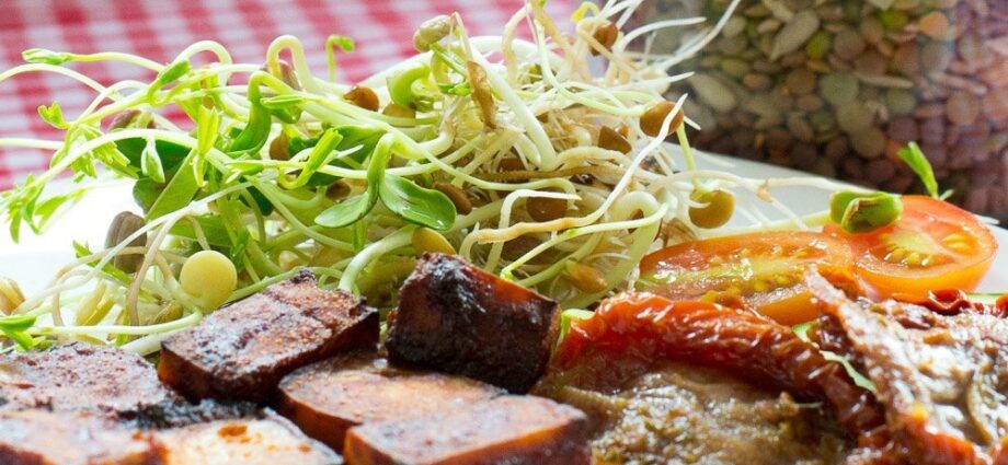 A red and white gingham cloth with a plate on it containing sprouts (from seed), tofu and sundried tomato