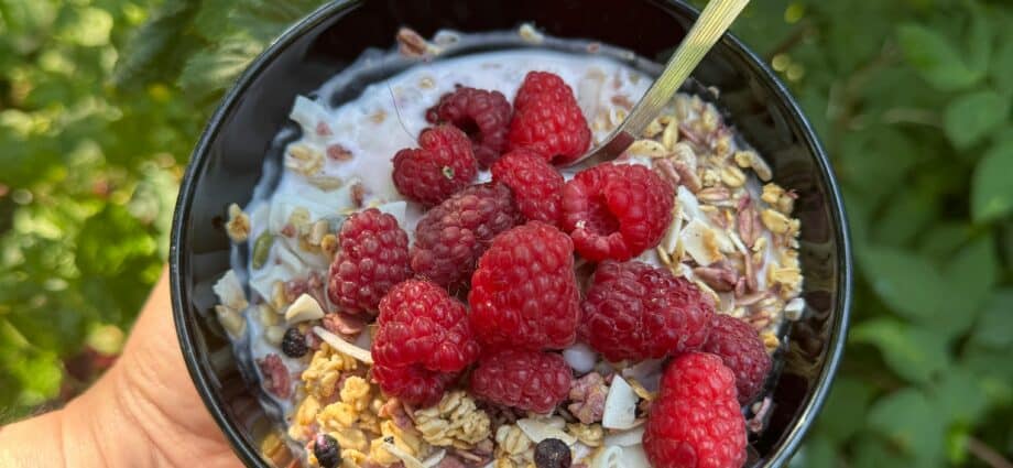 an upturned hand holding a black bowl containing oats topped with fresh raspberries