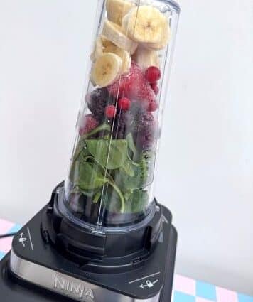 A blender cup filled with banana, frozen berries and spinach